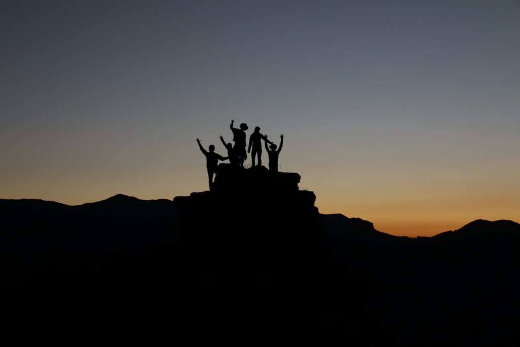 Grupo de individuos en la cima de una colina levantando las manos al atardecer.